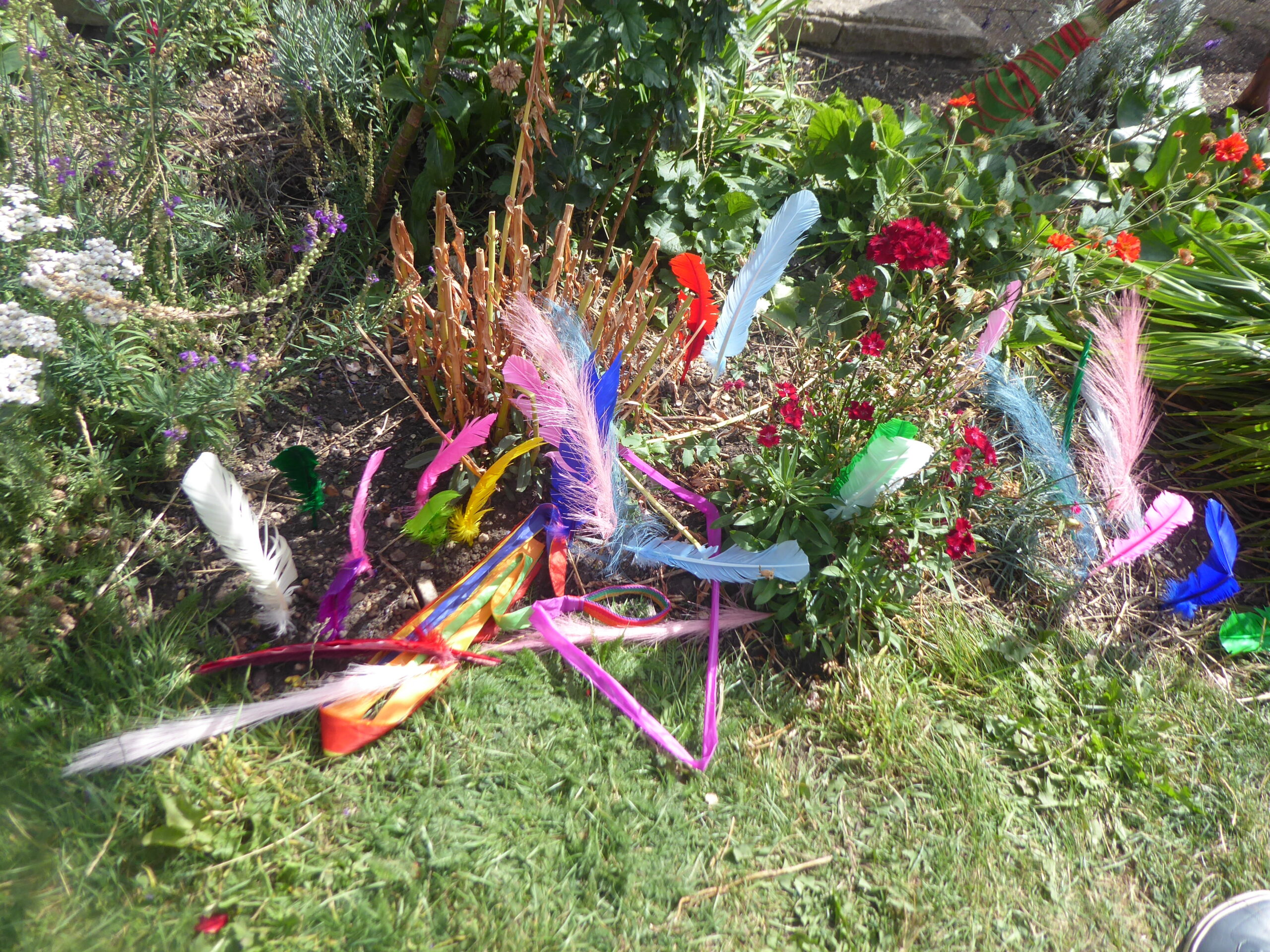 Feathers and fabric layered aroud flowers in the grass.