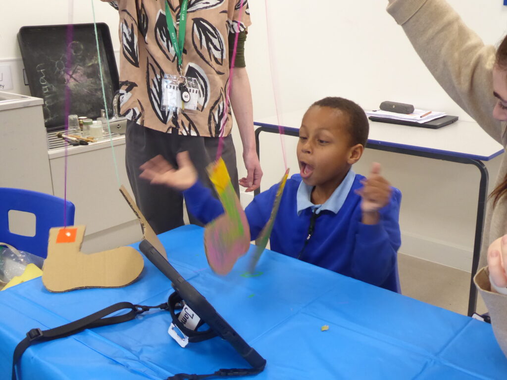 A SEND student on our:stories exploring stories through visual art. The artist holds carboard cutout shoes on string, like puppets. The student is smiling.