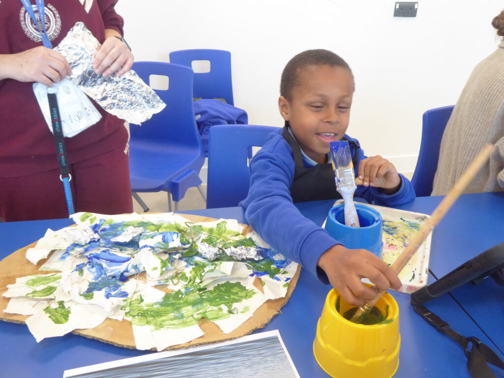 A SEND student explores reading through visual art. They sit at a table with paintbrushes and painting on top.