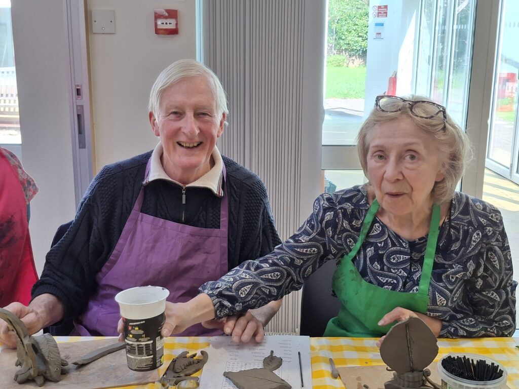 Two older adults taking part in a Create art:links ceramics workshop.
They are smiling.