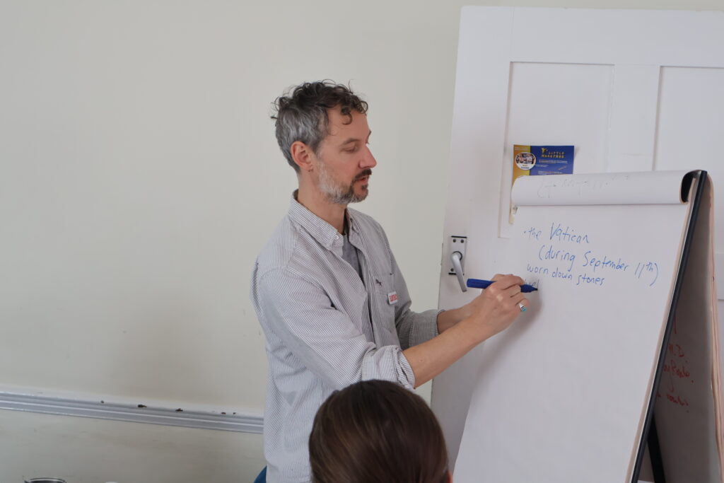 A man Create artist delivering a writing workshop. He is writing on a big piece of paper. art:links if our programme for older adults.