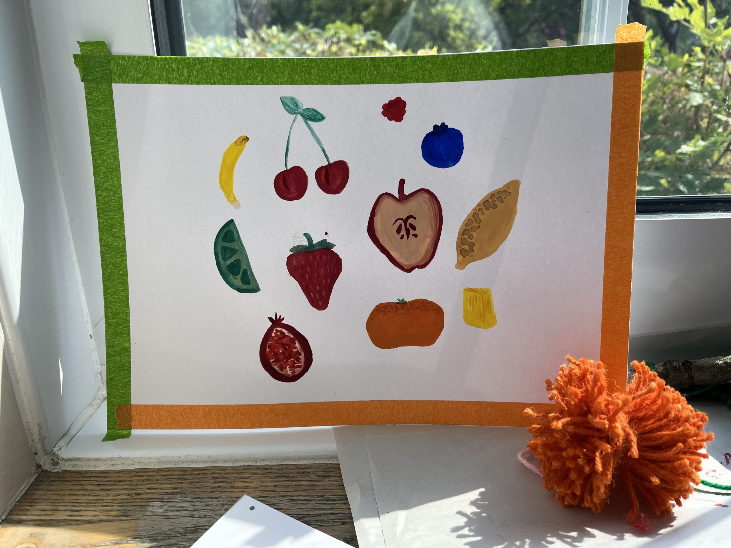 Colourful paintings of fruit on a piece of white paper with green and orange masking tape bordering the paper. Taken at a creative:tandem project